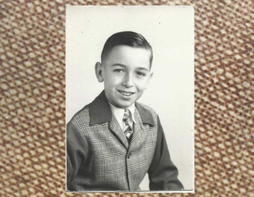 Rick Reefer at age 10. It's a black and white photograph and he is smiling and wearing a tweed jacket.