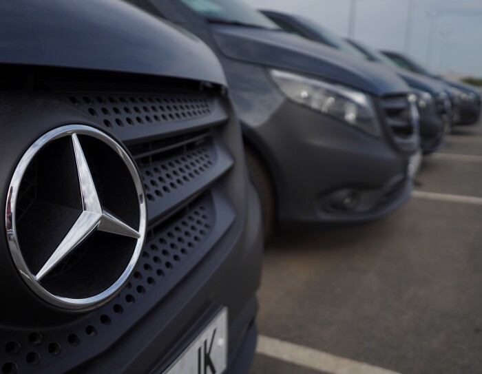 Una Mercedes Benz-Vans en un aparcamiento en primer plano. Detrás s even tres furgonetas más. En el primer plano se ve el logo de Mercedes-Benz.