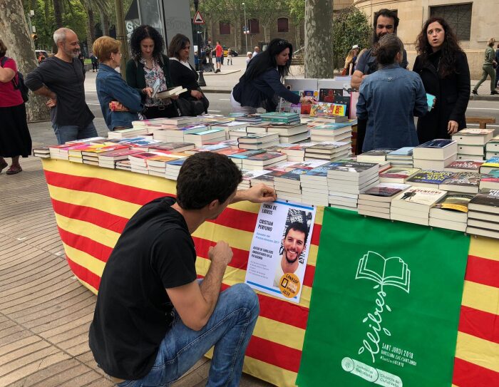Cristian Perfumo, el escritor de la Patagonia, está de rodillas enganchando un cartel promocional de la firma de sus libros para Sant Jordi en una mesa llena de libros también suyos.