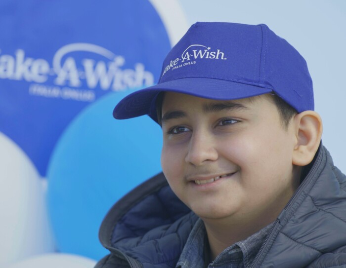 Hadi, uno dei bambini che hanno visto un desiderio realizzato grazie a Make-A-Wish, sorridente con un cappellino blu Make-a-Wish