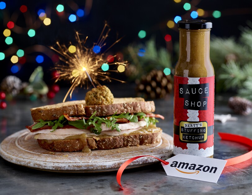 A sandich containing turkey and stuffing balls, next to the stuffing ketchup on a dinner table with an Amazon Label. There is also a sparkler sticking into the sandwich.
