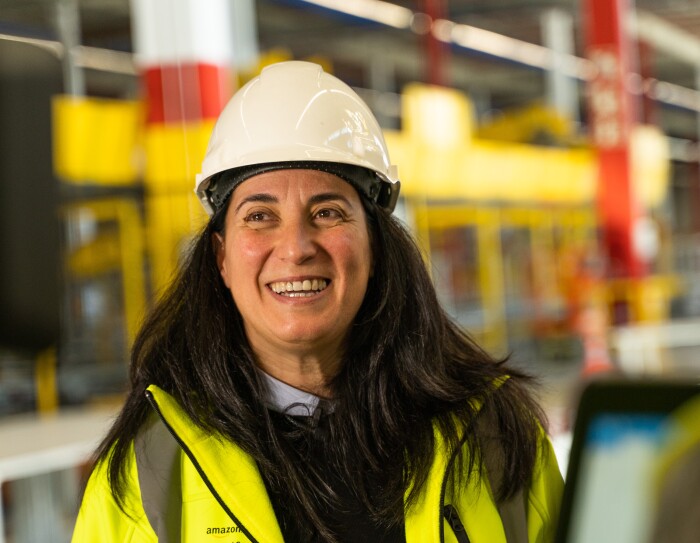 Sonia Corvera, Responsable Senior de Construcción para Amazon España, en primer plano y sonriendo con casco y chaleco amarillo. En un momento de la grabación.