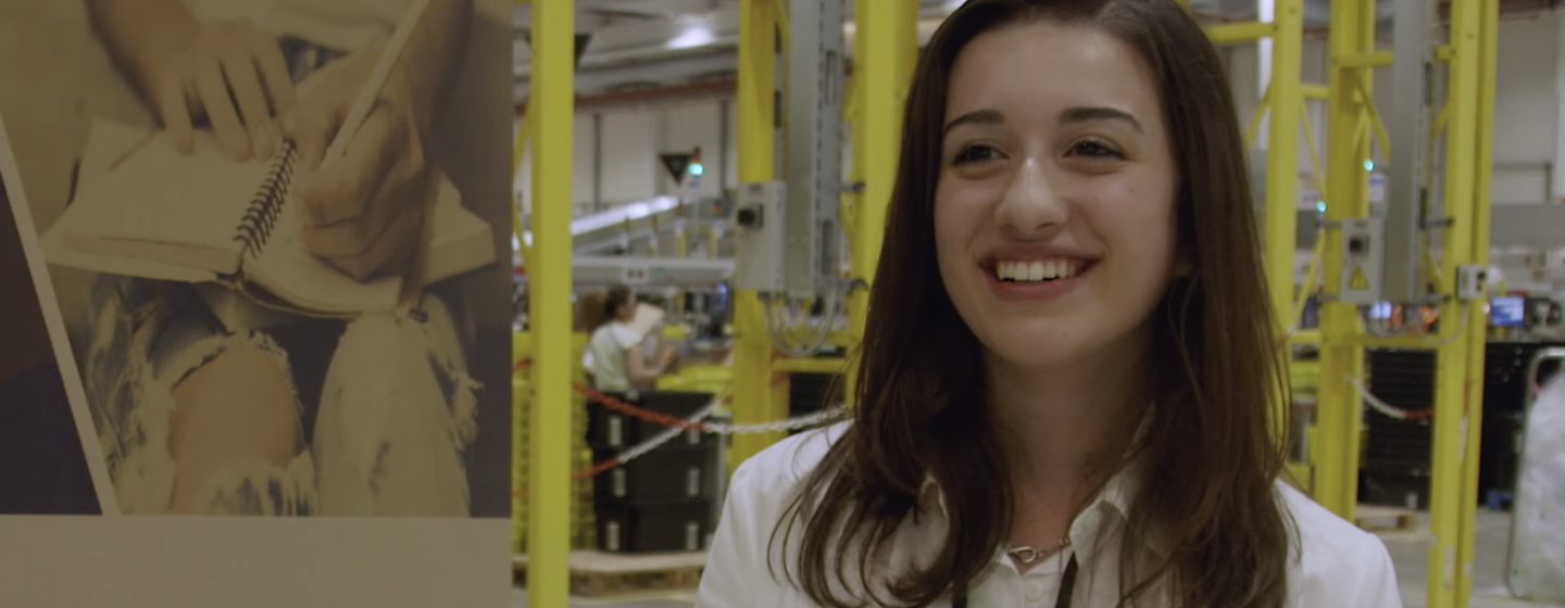Ritratto di una ragazza in un Centro di Distribuzione Amazon. Sullo sfondo, il Centro. La ragazza è una delle studentesse che hanno partecipato al concorso di scrittura indetto da Amazon nel piacentino.