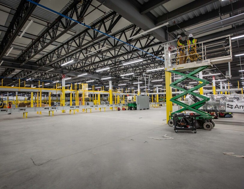 A crew works at building an Amazon Fulfillment center or warehouse in Cleveland, Ohio. Two men stand on a raised platform as they work on the ceiling