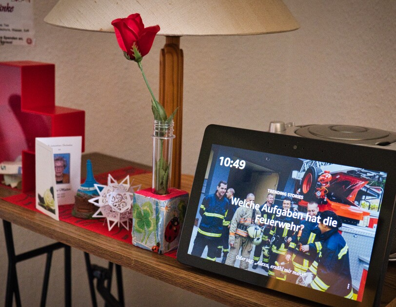 Auf einem kleinen Holztisch steht ein Amazon Echo Show an einen CD-Player angelehnt. Auf dem Tisch steht außerdem noch eine Rose, eine Karte und eine Spardose.