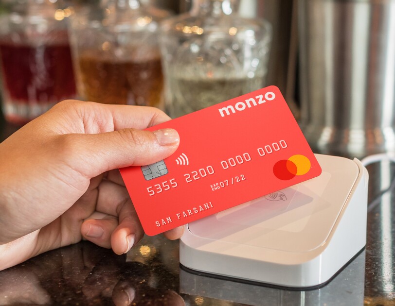 hand holding coral Monzo bank card over a white Apple pay machine