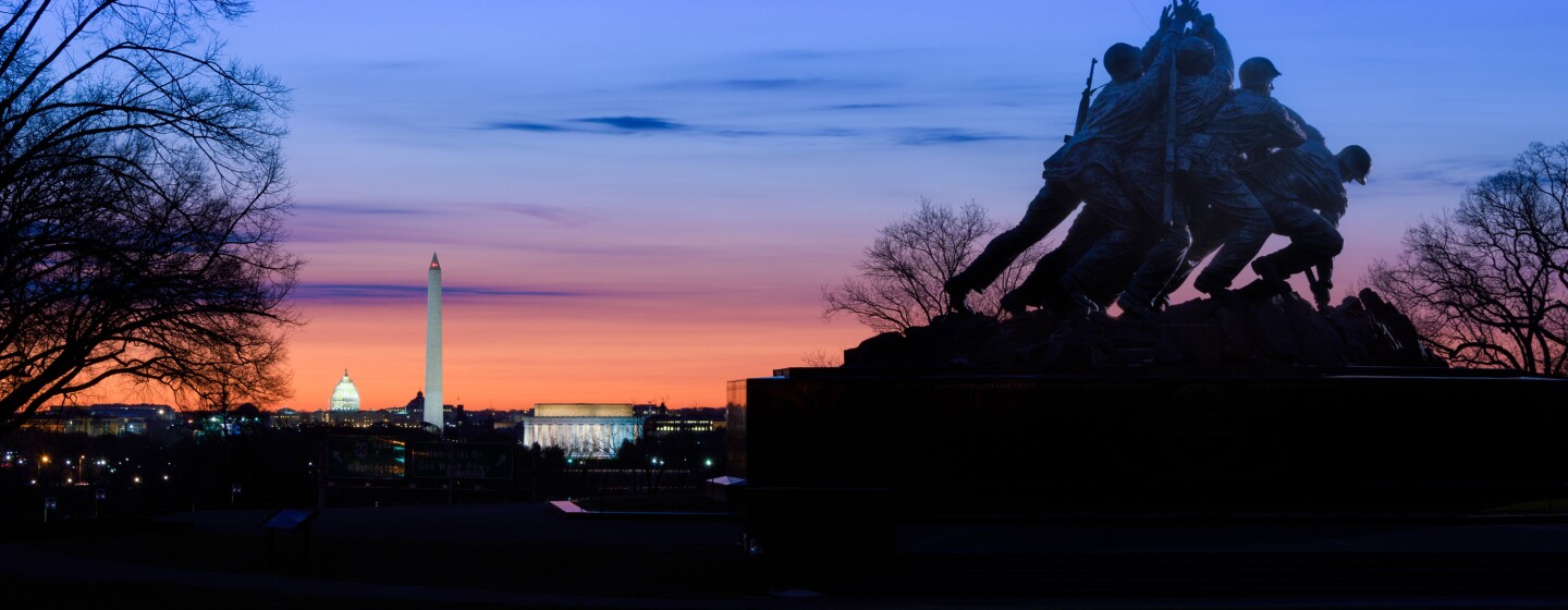 US Marine Corps War Memorial in front of a sunset with the Lincoln Memorial, Washington Monument, and US Capitol dome receding toward the horizon