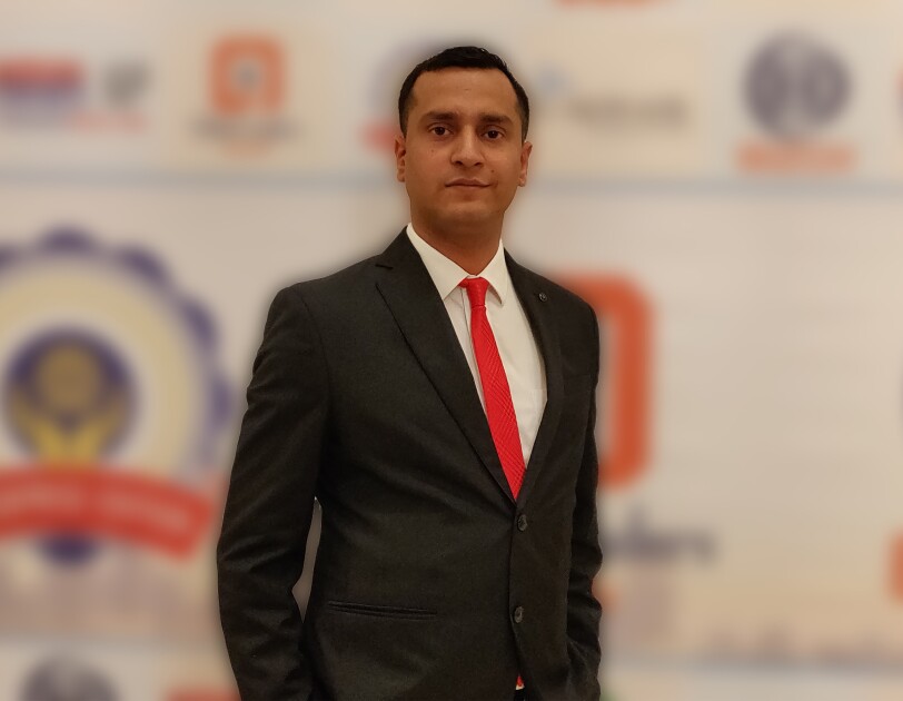 Jayant Jha, the CEO of Yantra stands across a banner in a formal suit
