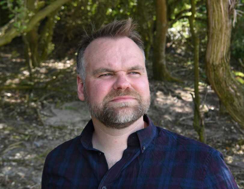 Headshot of David Atkinson standing in the woods, looking into the distance