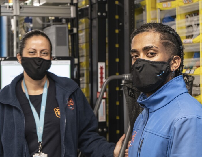 Jhon Steven Viafara Osorio y Adriana Osorio. Madre e hijo están situados delante de una estantería. Los dos van con mascarilla negra de Amazon y un polar azul. La madre polar azul oscuro y camiseta negra y el hijo polar azul claro abrochado. Los dos tienne la piel morena, la madre lleva el pelo recogido con un coleta y el hijo lleva trenzas.