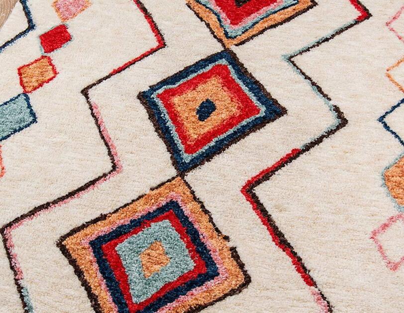Woven rug on a wood floor. Main color is ivory, with diamonds in navy, red, aqua, tangerine, and pink, framed by bi-color zig zags.