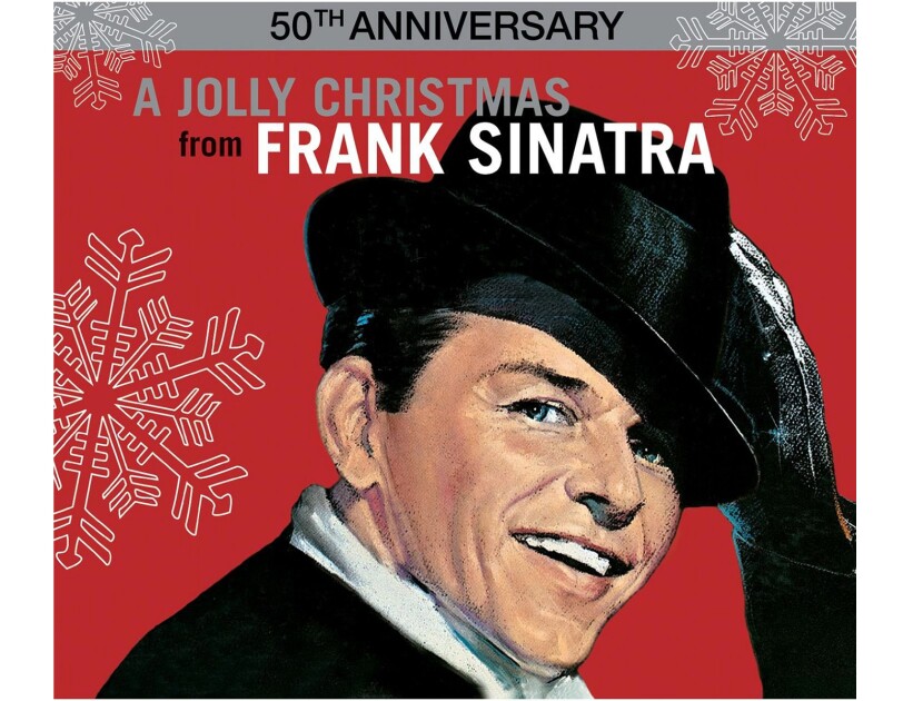 Frank Sinatra wears a suit and white button down, with a rimmed hat on his head, hair slicked, twinkle in his eye. His black gloved hand reaches up to tip his hat. He smiles toward the camera. The background is red, with large illustrated snowflakes falling around him.