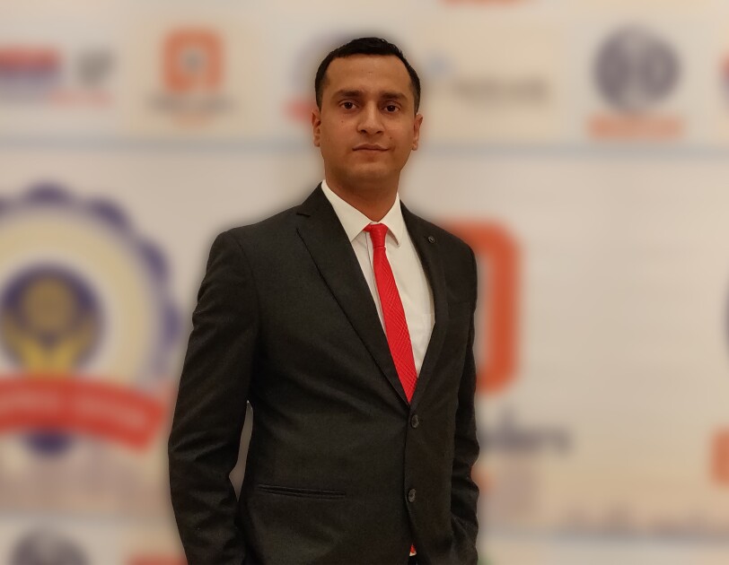 Jayant Jha, the CEO of Yantra stands across a banner in a formal suit