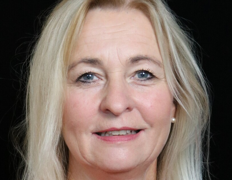 Eine Frau mit blonden Haaren und einer roten Bluse lächelt in die Kamera.