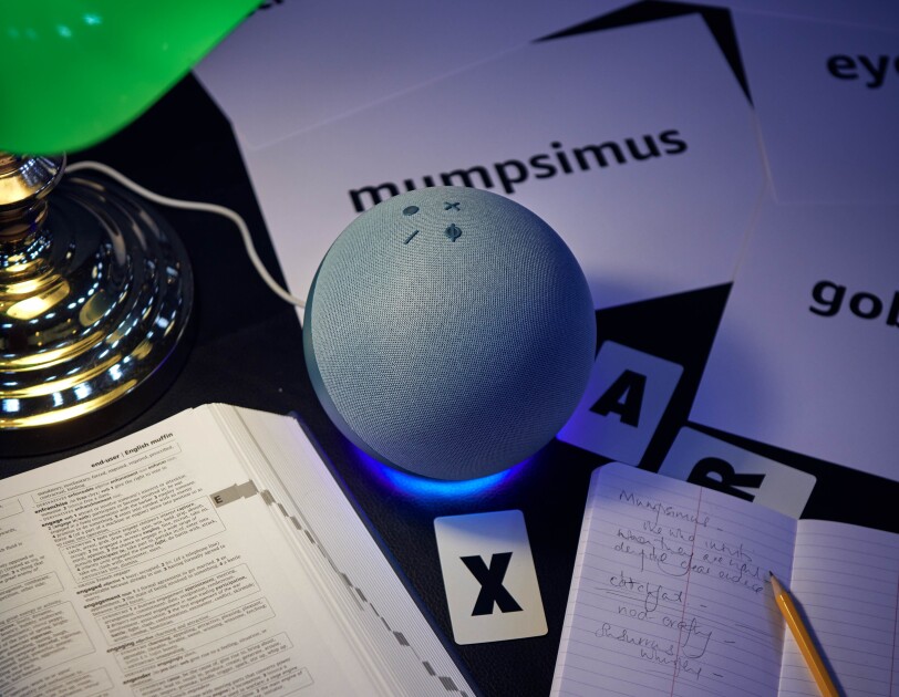 An Amazon Echo on a library table next to a dictionary and a notebook.