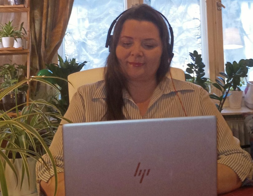 Eine Frau mit Kopfhörern sitzt an einem Tisch und schaut in ihren Laptop.