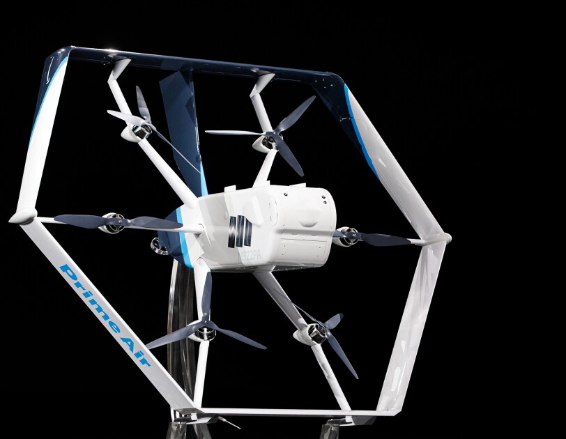 Biało-niebieski dron Prime Air na czarnym tle. Na środku drona widać sześć śmigieł i główny korpus.